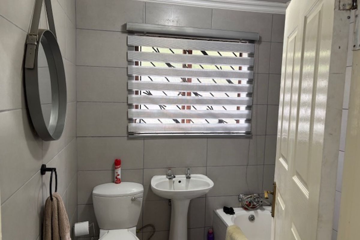 A functional bathroom featuring tiled walls, a pedestal basin, a toilet, and a bathtub with a window providing natural light.
