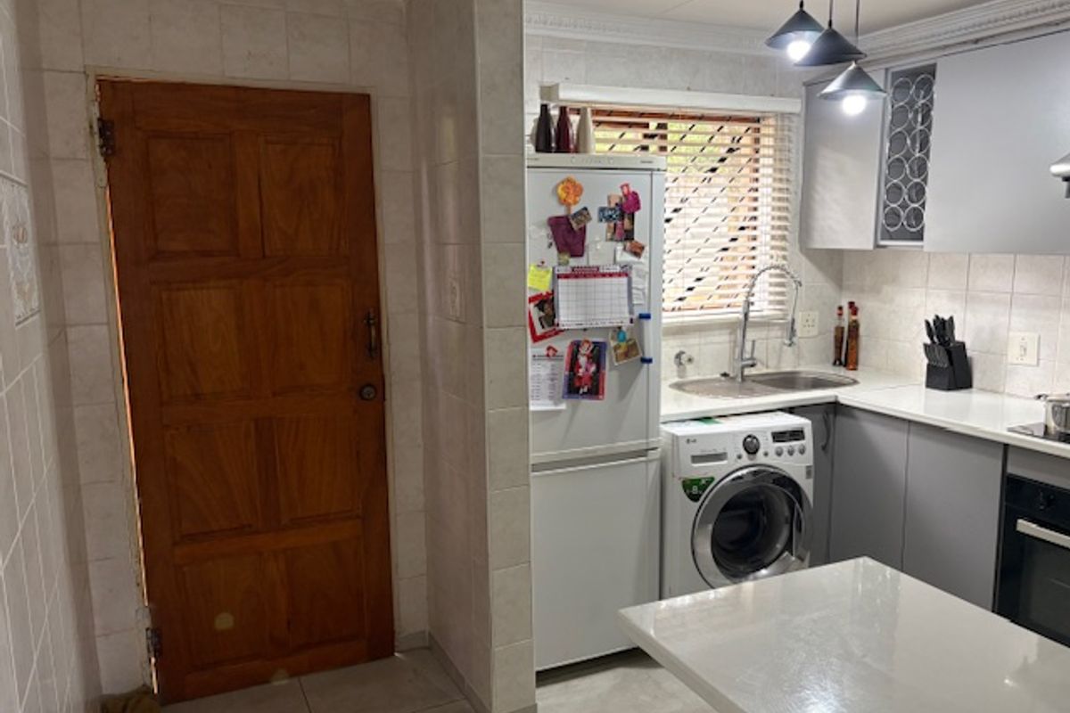 A functional kitchen featuring tiled splashbacks, built-in cabinetry, integrated oven, and a double sink with a convenient laundry appliance connection.