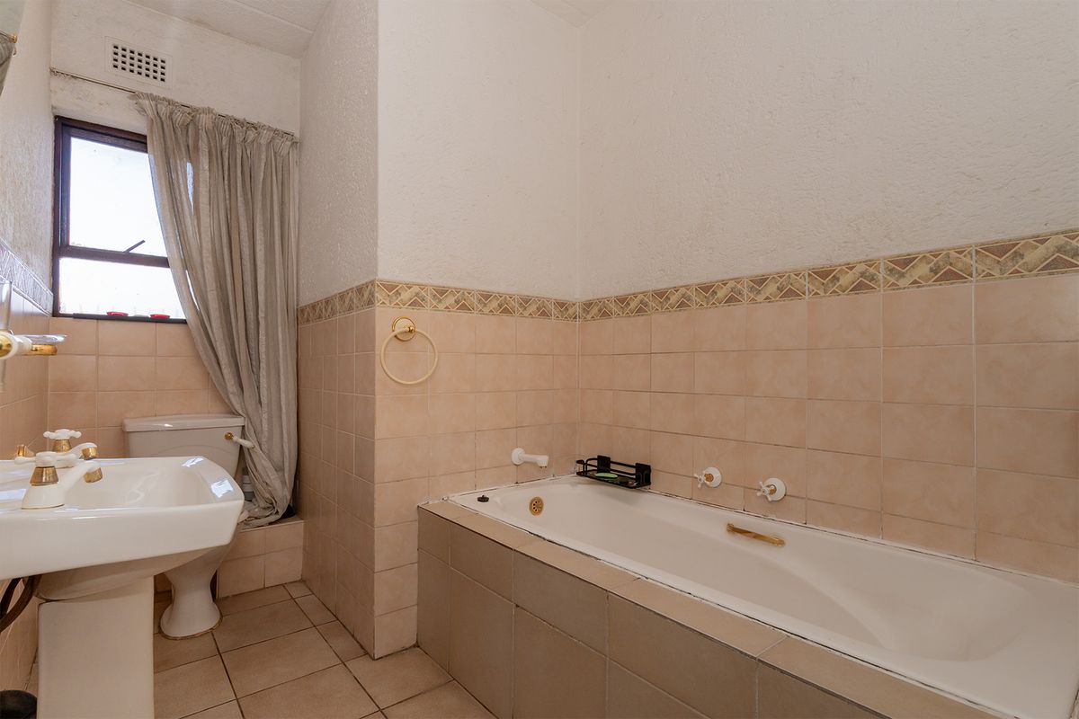 A dated bathroom featuring a built-in bathtub, pedestal sink, and ceramic wall tiling with a decorative border.