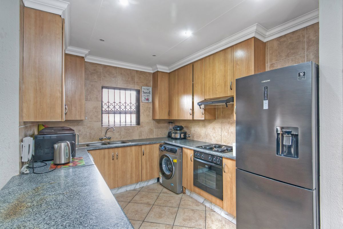 Functional kitchen featuring wood-finish cabinetry, granite countertops, tiled backsplash, and integrated appliances including an oven, hob, and extractor fan.