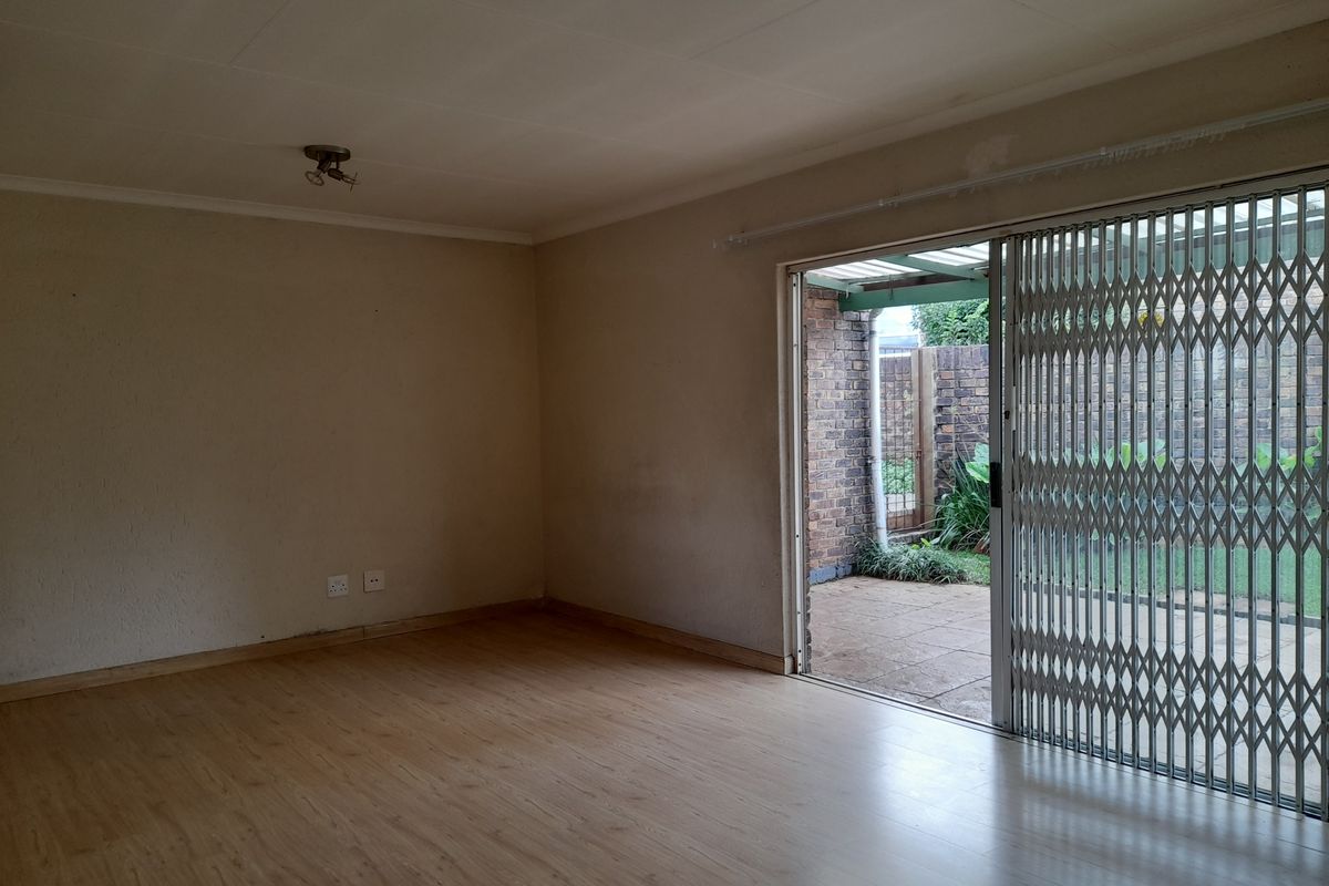 An empty living room featuring light wood-look laminate flooring and a sliding glass door with a security gate leading to a paved patio area.