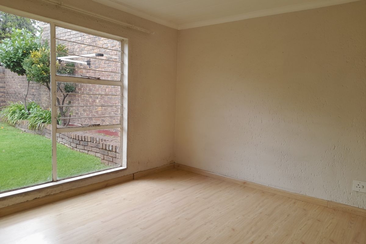 A vacant bedroom featuring light wood-look laminate flooring, textured walls, and a large window overlooking a private garden area.