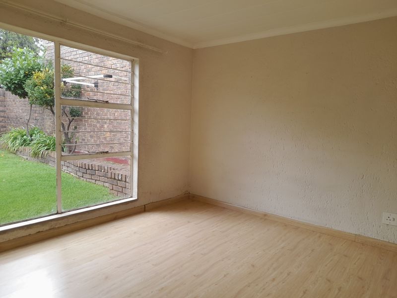 A vacant bedroom featuring light wood-look laminate flooring, textured walls, and a large window overlooking a private garden area.