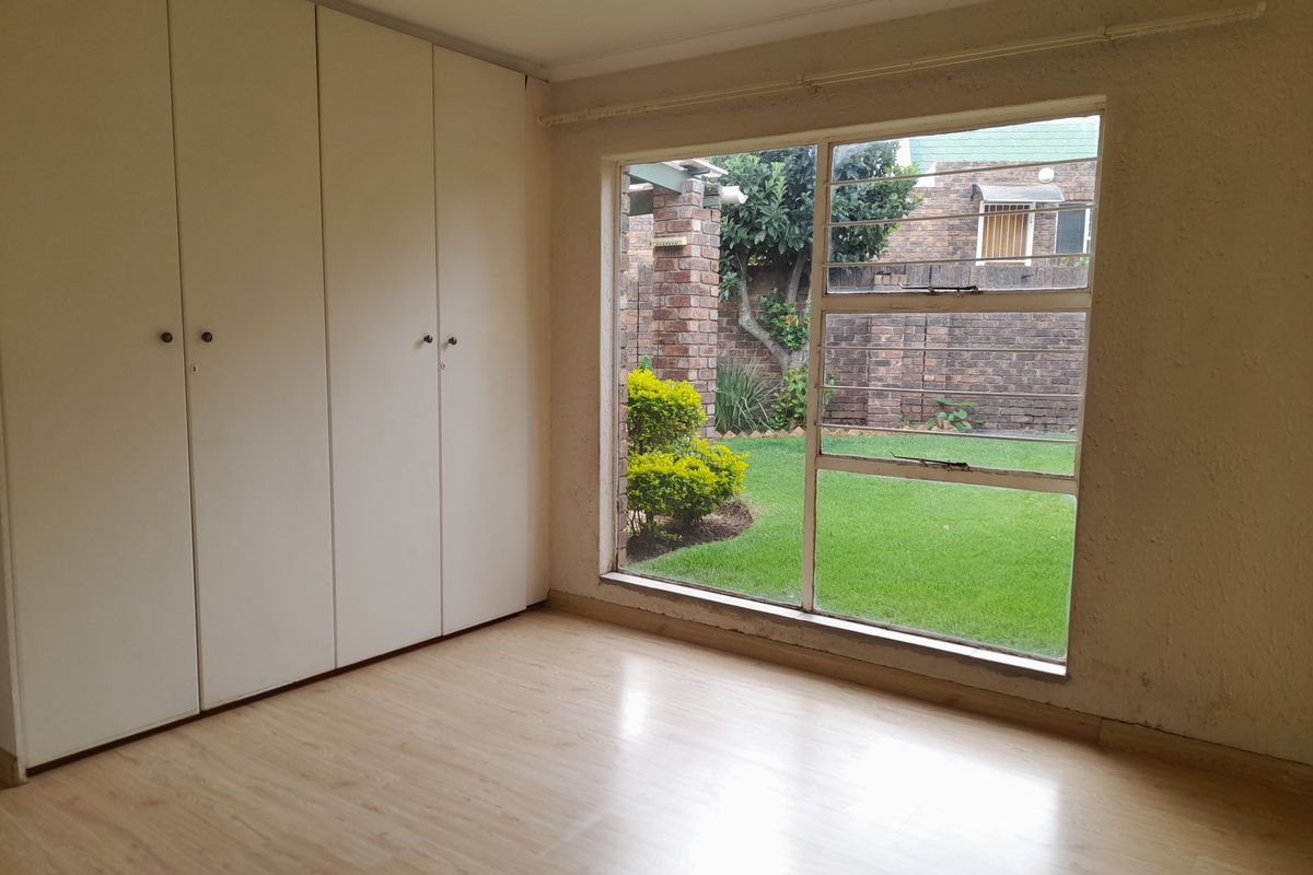 A bright bedroom featuring built-in cupboards, light wood-look flooring, and a large window overlooking the private garden.