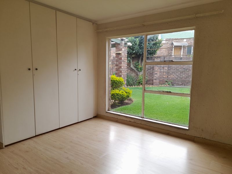 A bright bedroom featuring built-in cupboards, light wood-look flooring, and a large window overlooking the private garden.