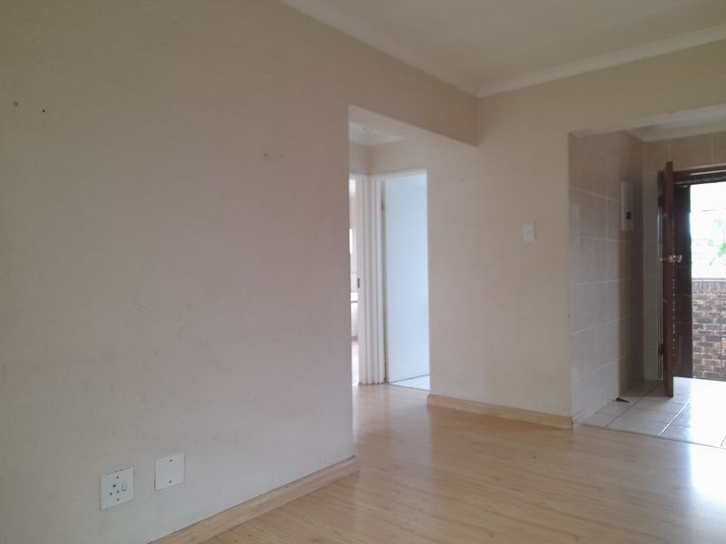 An interior view of a living area featuring light wood-look laminate flooring, neutral wall tones, and a doorway leading to an exterior entrance.