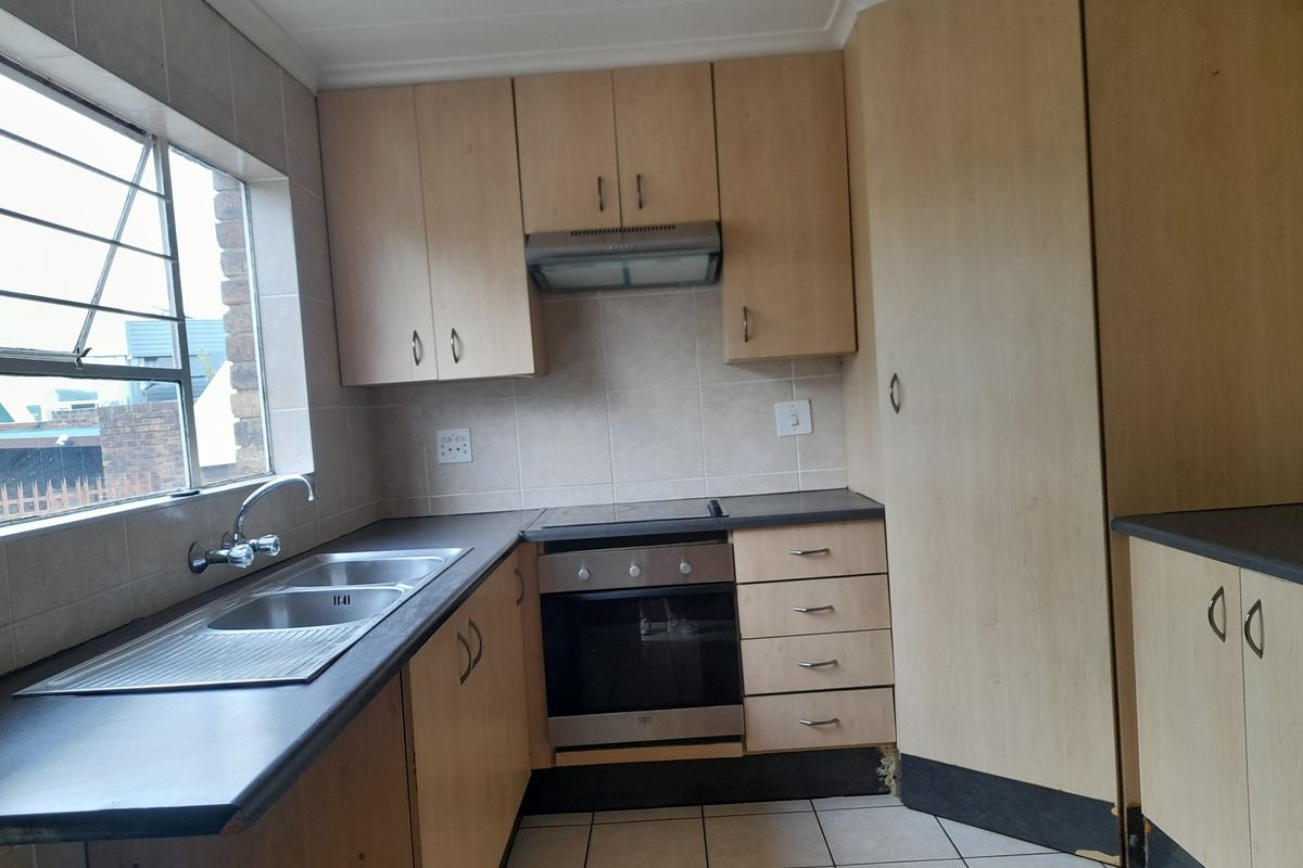 A functional kitchen featuring light wood cabinetry, a built-in oven with hob, extractor fan, and a double stainless steel sink with tiled splashbacks.