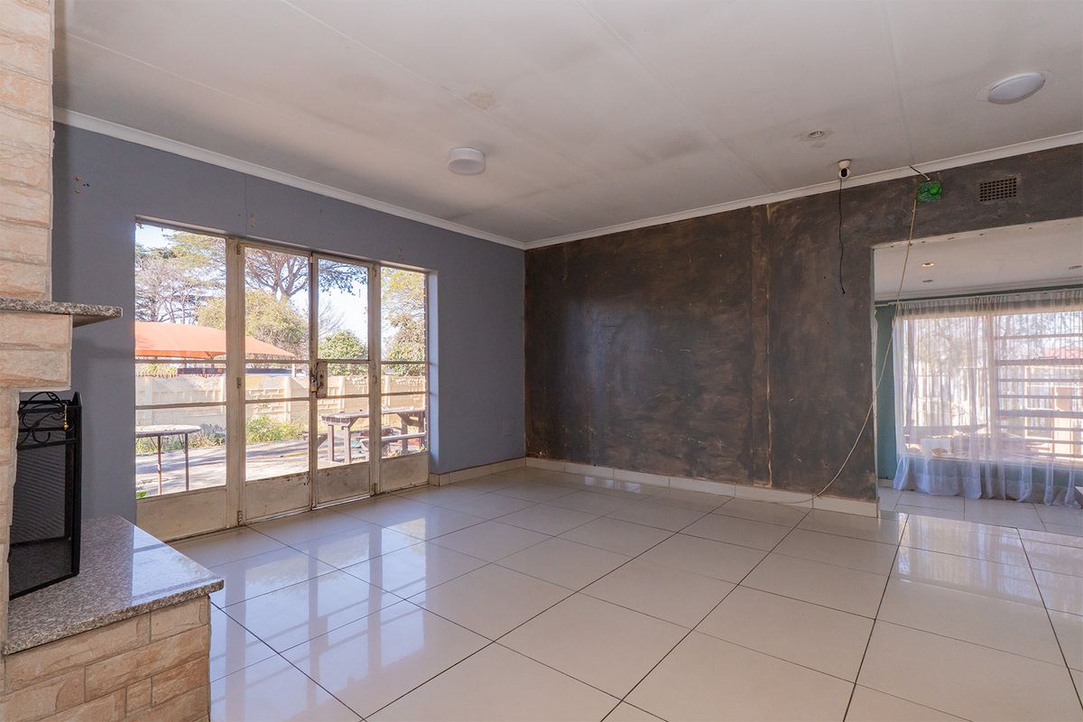 An empty living room featuring large sliding glass doors, tiled flooring, and a brick fireplace, currently requiring cosmetic wall and ceiling repairs.