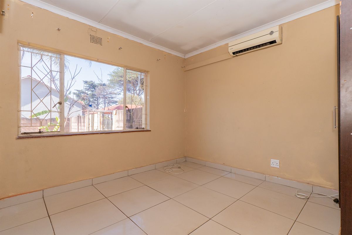 An empty bedroom featuring tiled flooring, an air conditioning unit, and security bars on the window, ready for a fresh coat of paint.