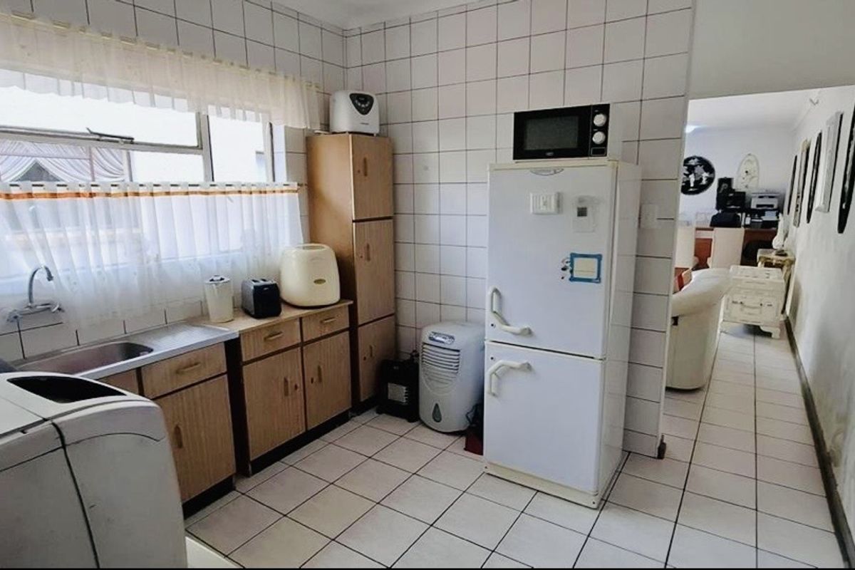 A functional kitchen area featuring tiled walls, built-in wooden cabinetry, a stainless steel sink, and direct access to the adjacent living space.