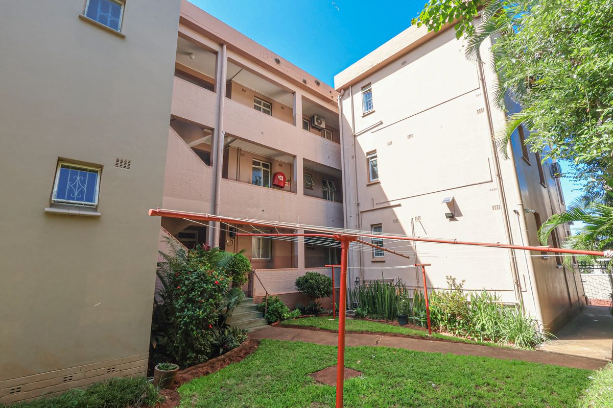 A view of the apartment building exterior featuring a shared courtyard, landscaped garden area, and multi-level access balconies.