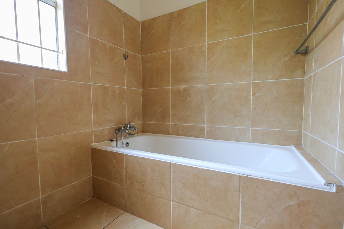 A functional bathroom featuring a built-in bathtub with beige wall tiling and a window with security bars.