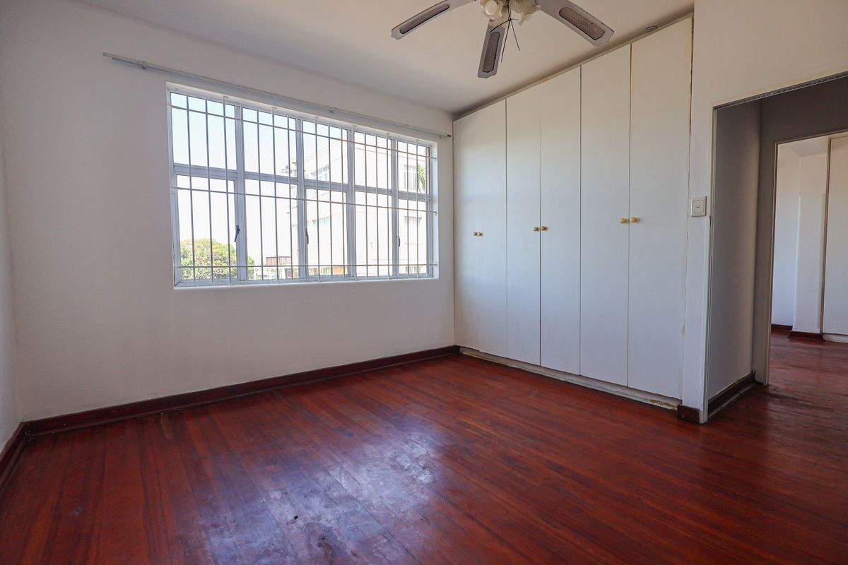 A bedroom featuring polished timber flooring, built-in wardrobes, a ceiling fan, and large windows with security bars.
