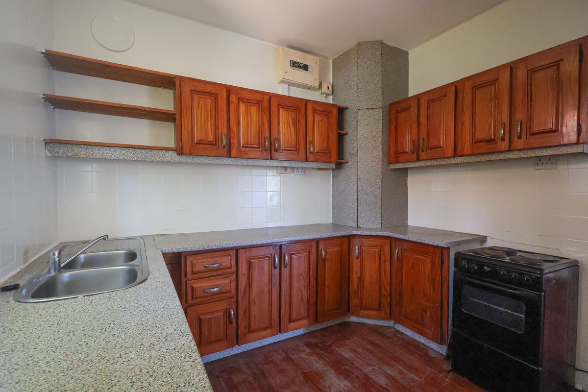 A dated kitchen featuring wooden cabinetry, laminate countertops, a double-basin stainless steel sink, and a freestanding stove.