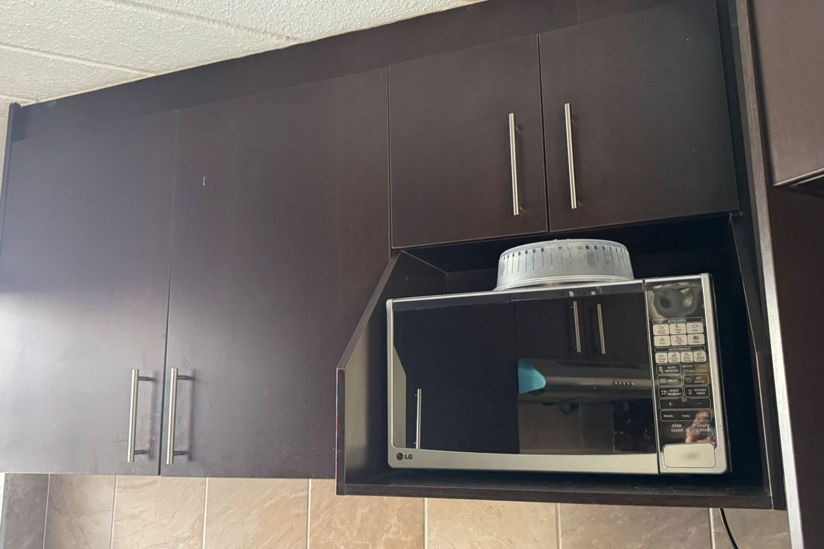 Close-up view of dark wood kitchen cabinetry featuring a dedicated built-in microwave shelf and neutral tiled backsplash.
