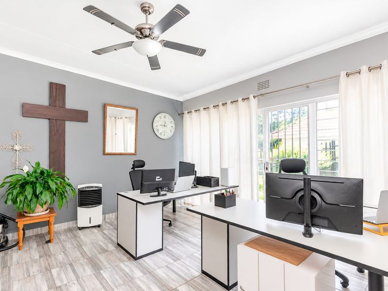 A bright and functional home office featuring tiled flooring, a ceiling fan, and large sliding glass doors providing natural light and garden access.