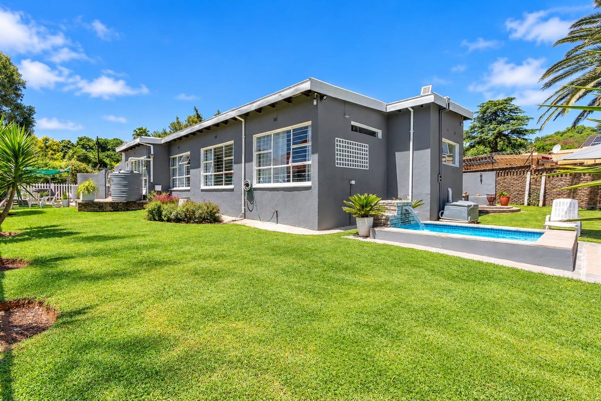 Rear view of the property featuring a well-maintained lawn, a swimming pool with a water feature, and a water storage tank.