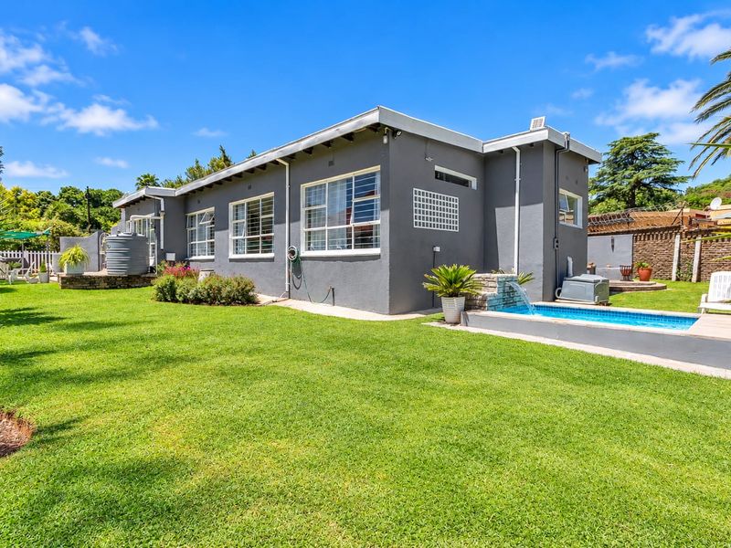 Rear view of the property featuring a well-maintained lawn, a swimming pool with a water feature, and a water storage tank.