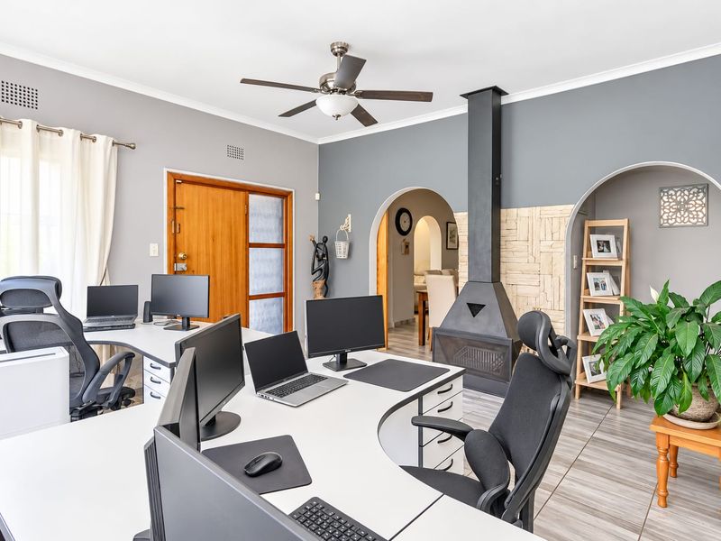 A spacious home office featuring a modern freestanding fireplace with stone cladding, arched architectural details, and tiled flooring.