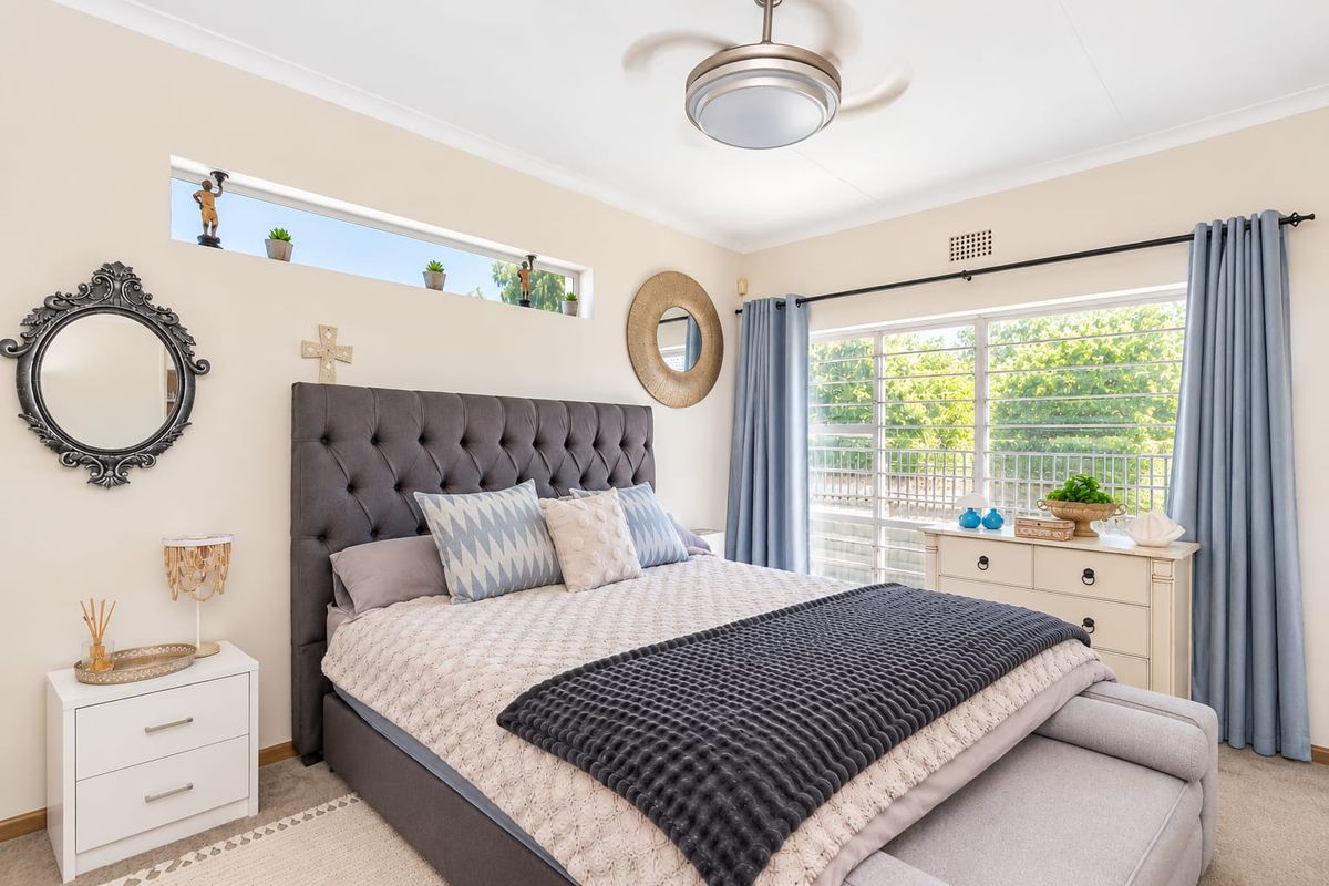 A well-maintained bedroom featuring a ceiling fan, large window with natural light, and a high-level clerestory window.