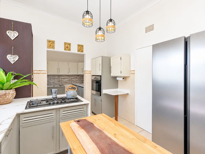 A well-maintained kitchen featuring a gas cooktop, built-in oven, stone countertops, and pendant lighting, with an open transition to a secondary scullery area.