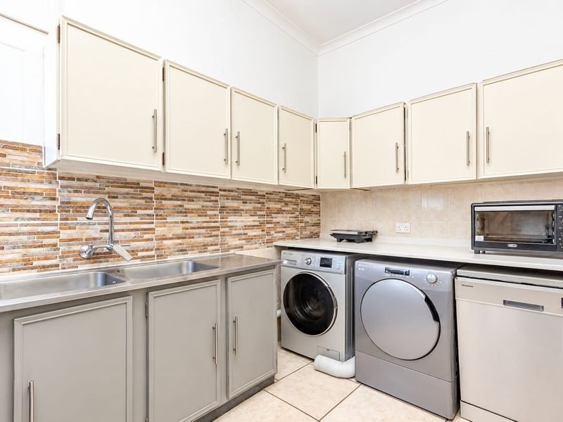 Functional laundry room featuring built-in cabinetry, double stainless steel sink, tiled splashback, and dedicated space for laundry appliances.