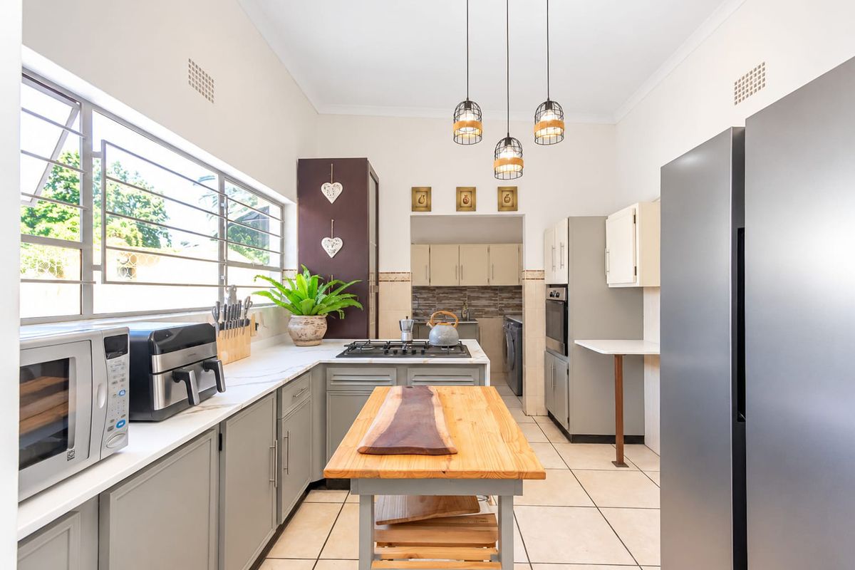 Modern kitchen featuring grey cabinetry, stone countertops, gas hob, built-in oven, and tiled flooring, with an adjacent scullery area.