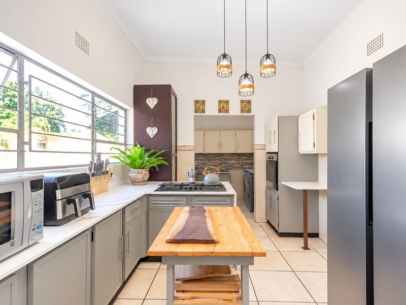 Modern kitchen featuring grey cabinetry, stone countertops, gas hob, built-in oven, and tiled flooring, with an adjacent scullery area.