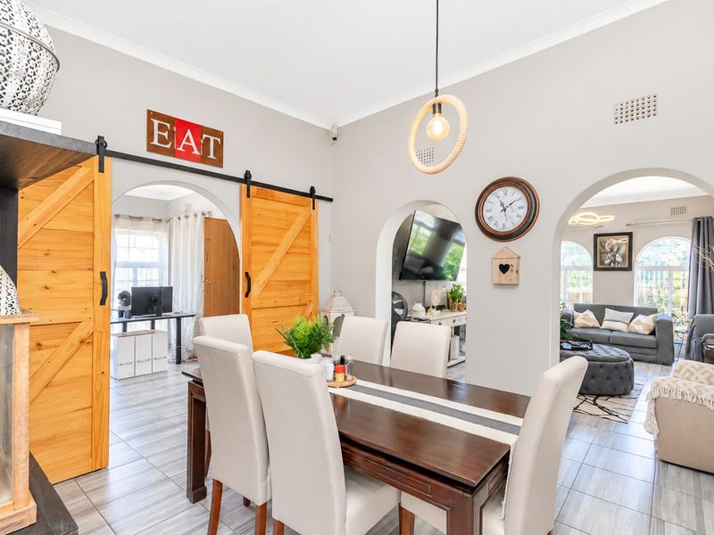 A well-lit dining room featuring arched doorways, sliding barn doors, and modern tiled flooring, providing an open and connected flow to adjacent living spaces.