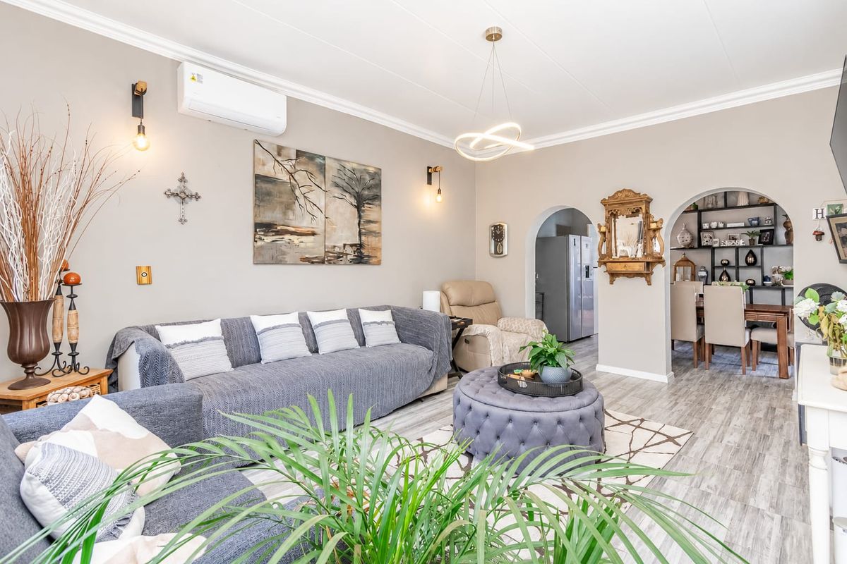 A well-maintained living room featuring modern laminate flooring, an archway leading to the dining area, and a wall-mounted split-system air conditioner.