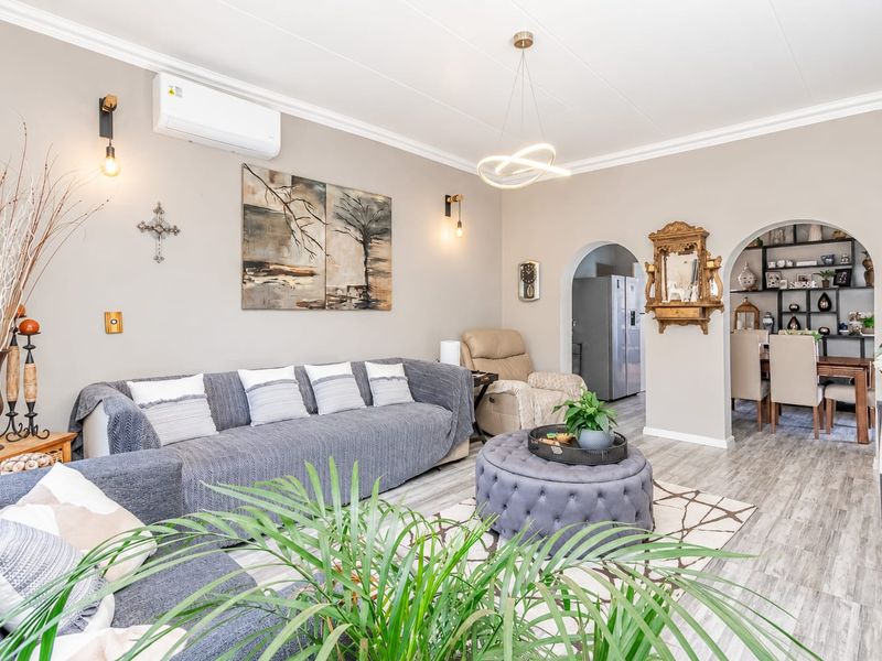 A well-maintained living room featuring modern laminate flooring, an archway leading to the dining area, and a wall-mounted split-system air conditioner.