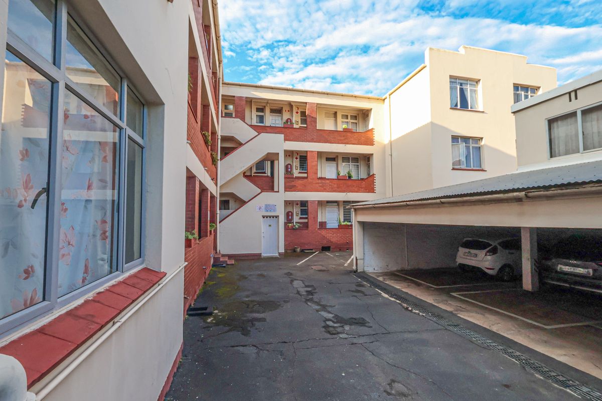 Exterior view of the apartment complex courtyard featuring brick facade, external stairwell, and covered parking bays.
