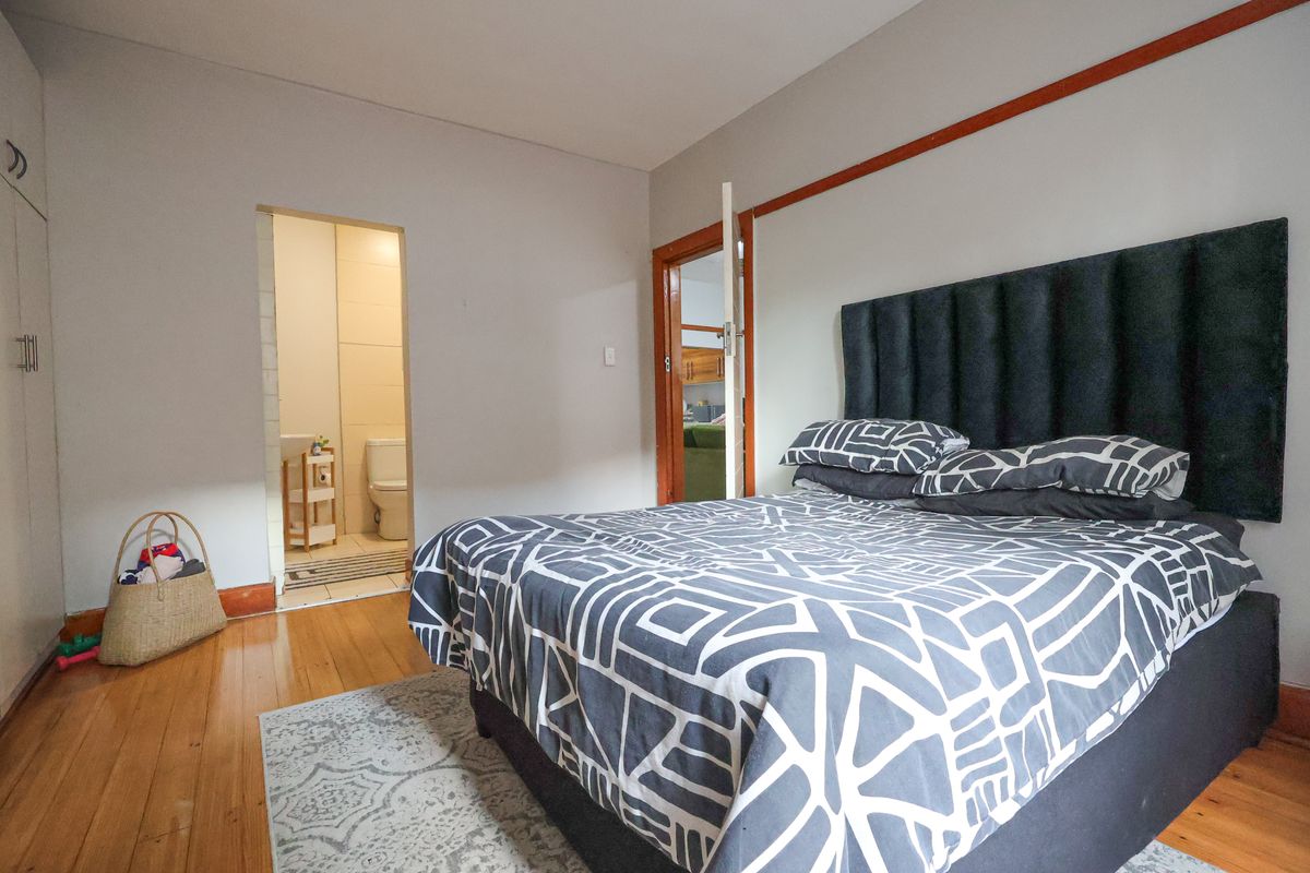 A bedroom featuring polished wooden floors, built-in cupboards, and an en-suite bathroom with tiled finishes.