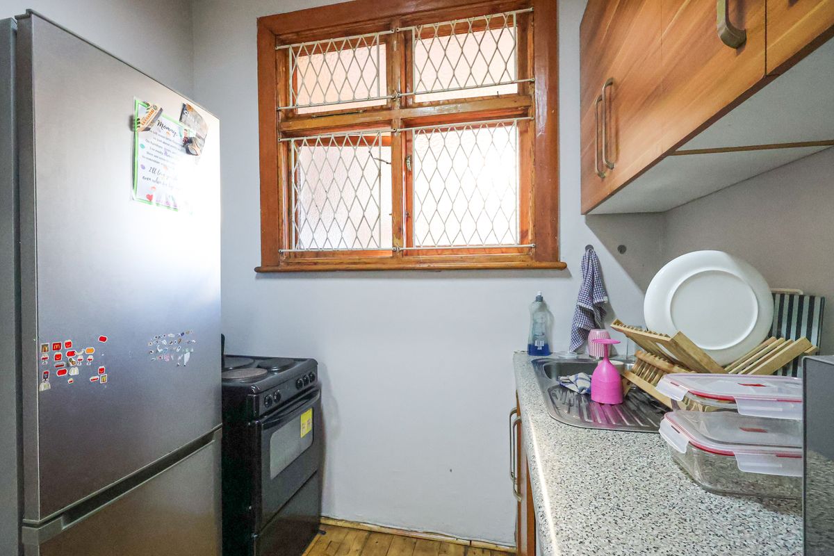 A compact kitchen featuring laminate countertops, wooden cabinetry, a stainless steel sink, and a wooden window frame with security bars.