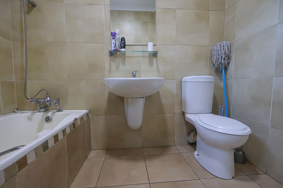 A functional bathroom featuring a pedestal basin, a standard toilet, and a bathtub with a shower mixer, finished with neutral wall and floor tiles.