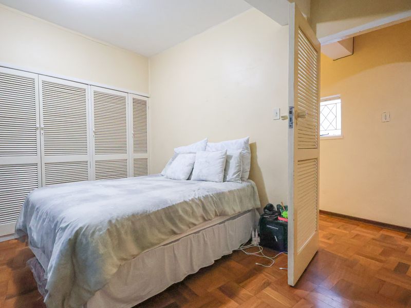 A bedroom featuring built-in louvered closet doors and parquet flooring, with an open doorway leading to an adjacent space.