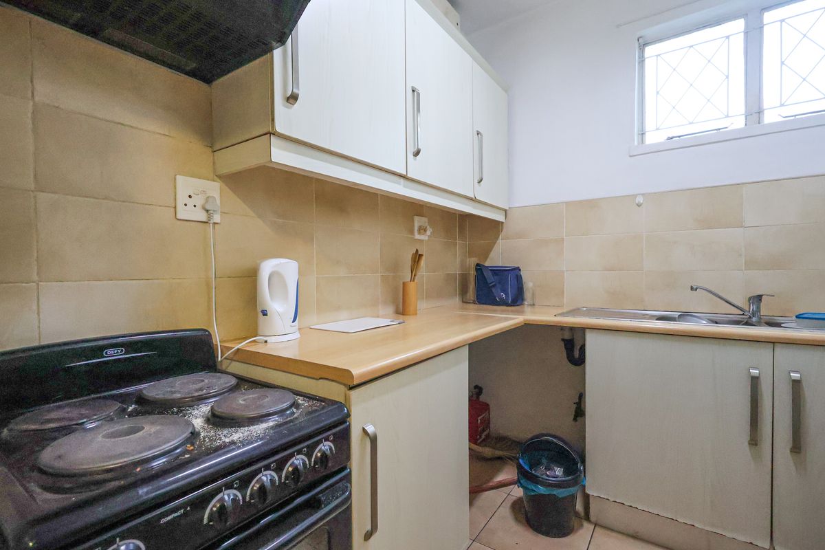 A compact kitchen featuring built-in cabinetry, a freestanding stove with extractor fan, tiled splashbacks, and a stainless steel sink.