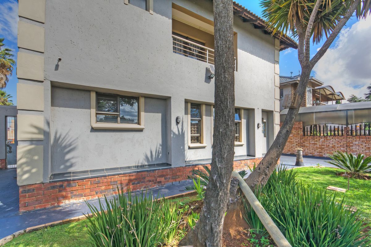 Side elevation of a two-story residential property featuring a balcony, brick base detailing, and landscaped garden area.