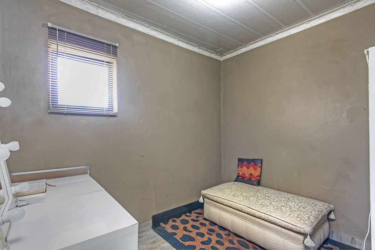 A small bedroom featuring neutral-toned walls, a window with fitted blinds, and a simple ceiling finish.