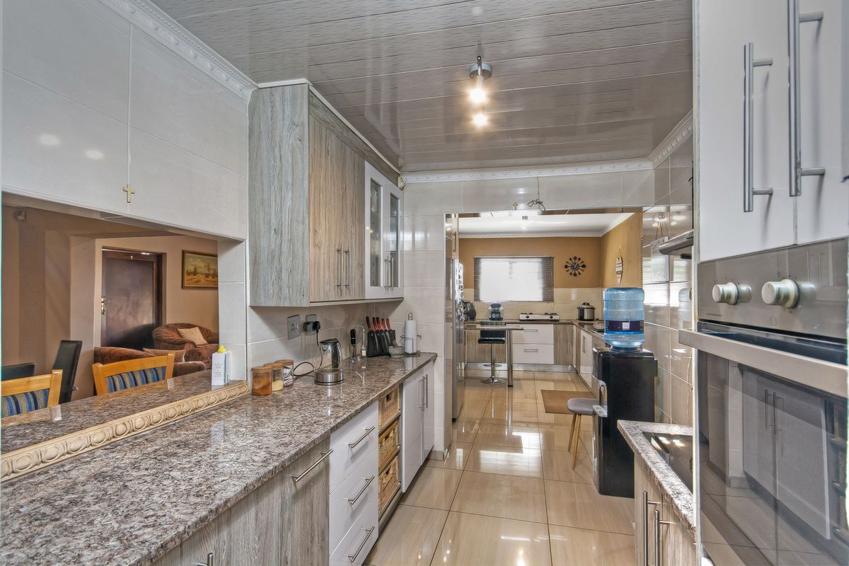 A functional kitchen featuring granite countertops, built-in oven, and tiled flooring, with an open-plan layout connecting to the adjacent living area.