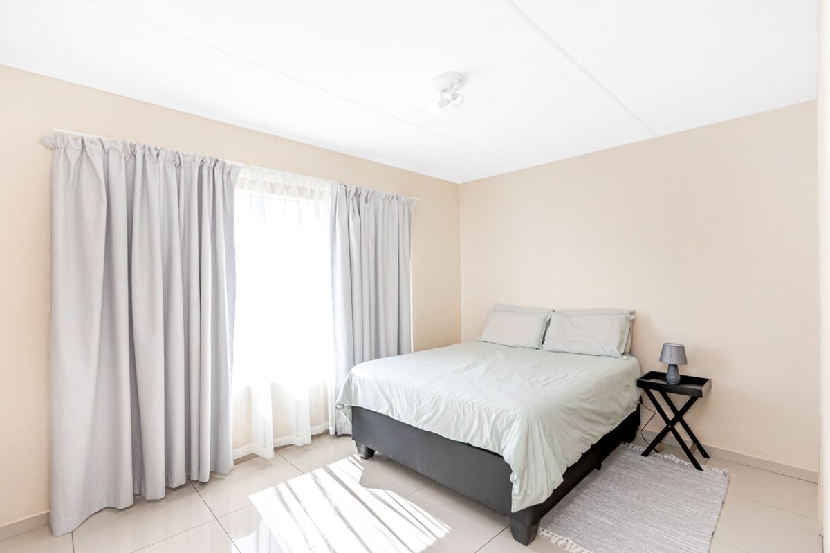 A bright and neutral bedroom featuring tiled flooring and large windows with floor-to-ceiling curtains.