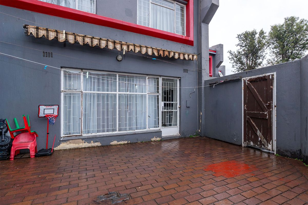Rear exterior area featuring brick paving, a retractable awning, and direct access to the home through a security-fitted door and window.