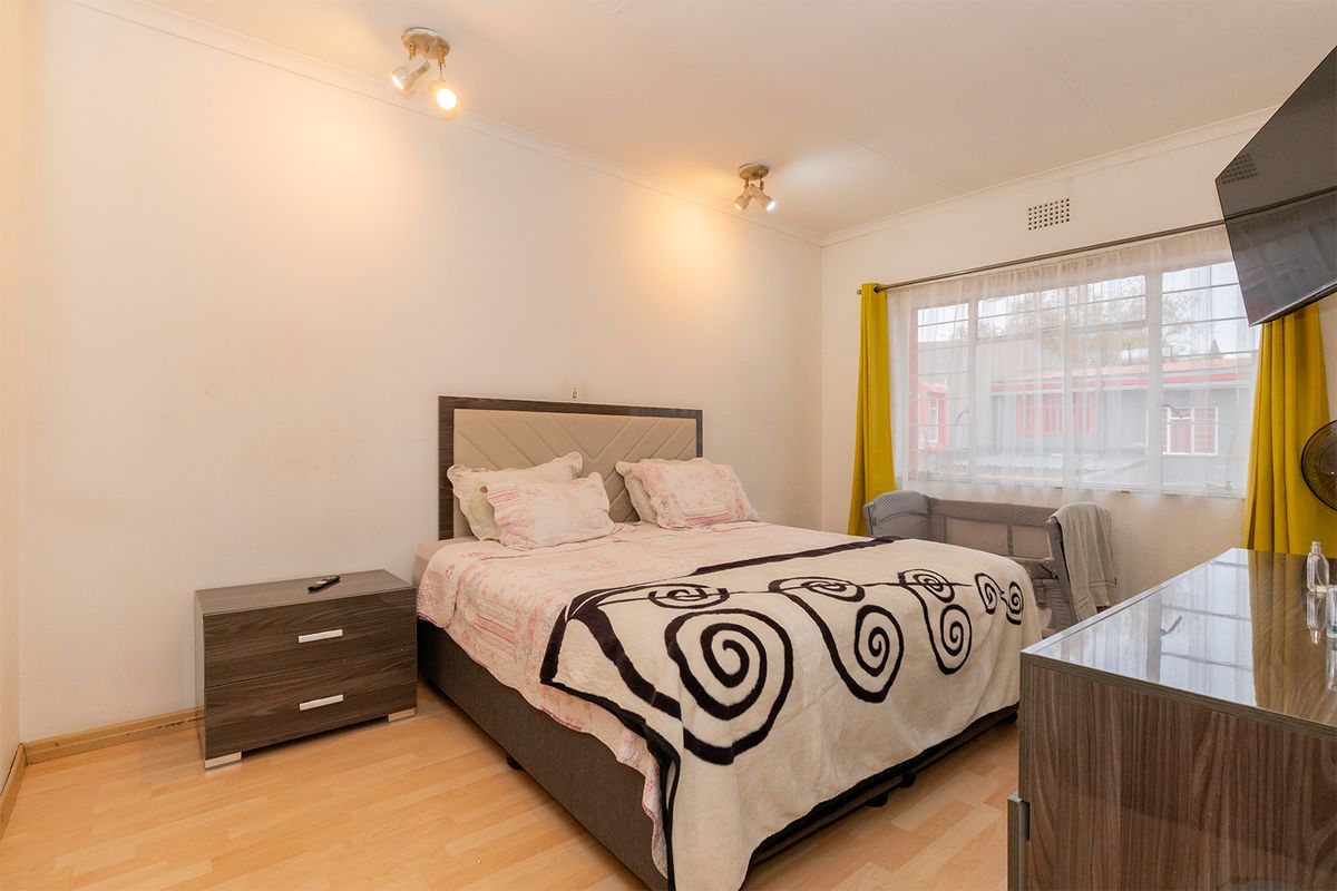 A well-lit bedroom featuring laminate flooring, neutral walls, and a large window providing natural light.