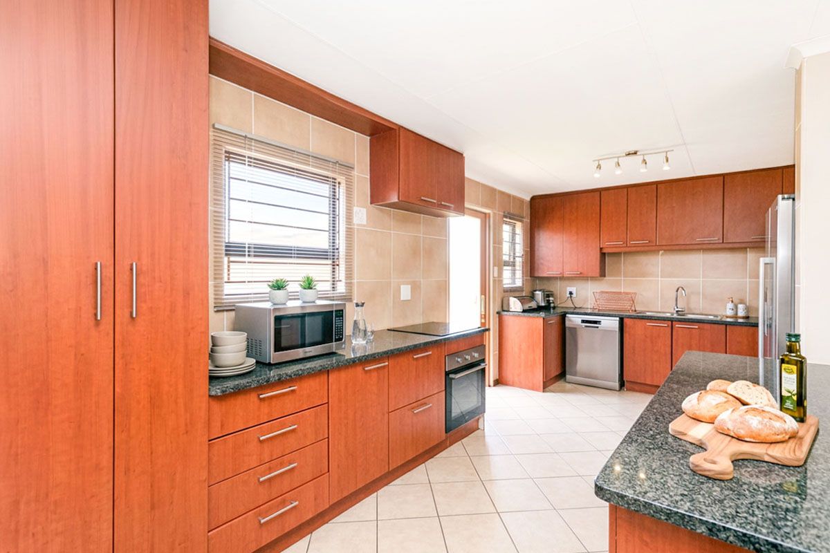 A functional kitchen featuring wood-finish cabinetry, granite countertops, tiled backsplash, and integrated appliances including an oven, hob, and dishwasher.