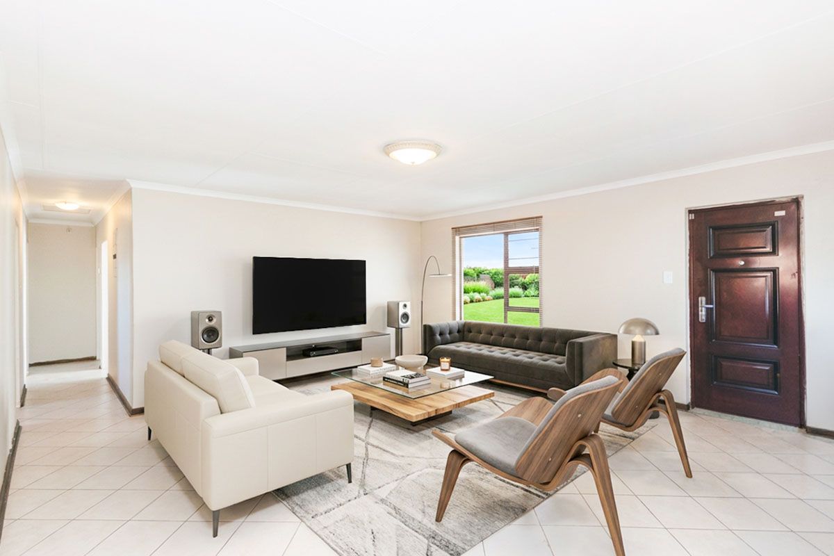 A bright and spacious living room featuring neutral tiled flooring, large windows with garden views, and a solid timber entrance door.
