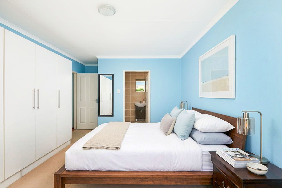 A well-maintained bedroom featuring built-in wardrobes, neutral carpeting, and an en-suite bathroom with tiled finishes.