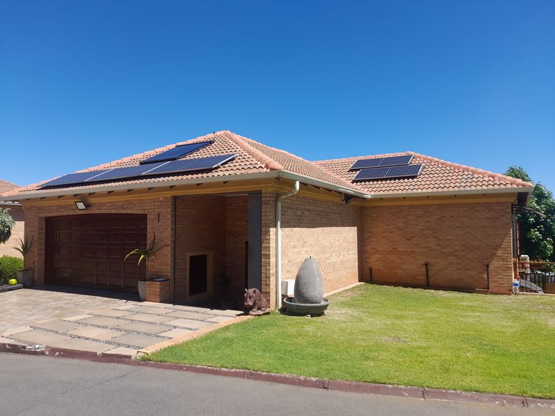 Front elevation of a facebrick cluster home featuring a tiled roof, integrated solar panels, a double garage, and a well-maintained front lawn.