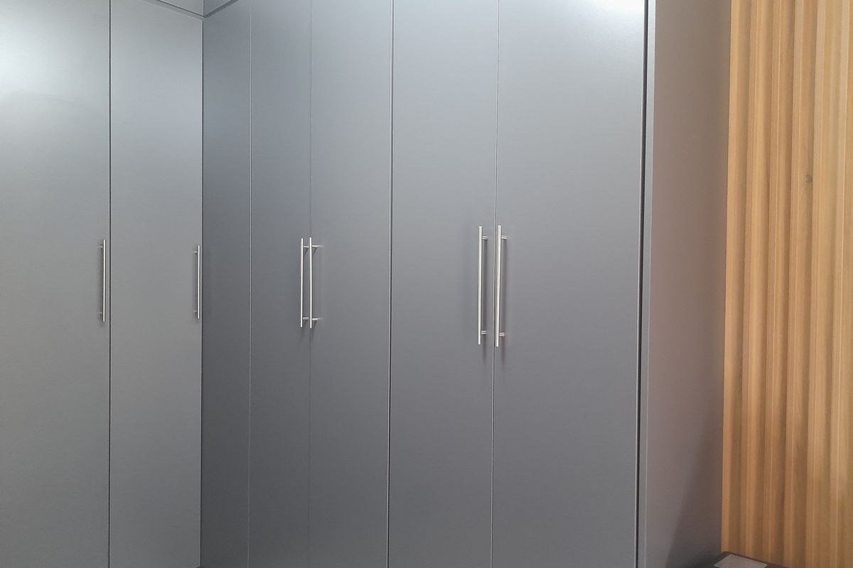 A modern bedroom featuring sleek grey built-in cupboards and decorative vertical wood slat wall paneling.