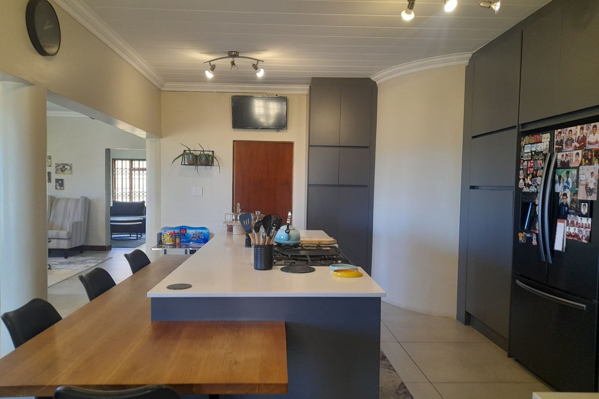 Modern kitchen featuring a central island with a gas hob, integrated cabinetry, and tiled flooring, flowing into an adjacent living area.