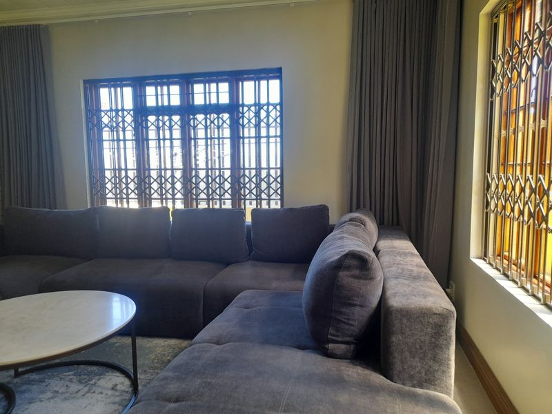 A comfortable living room featuring large windows with fitted security gates and floor-to-ceiling curtain tracks.